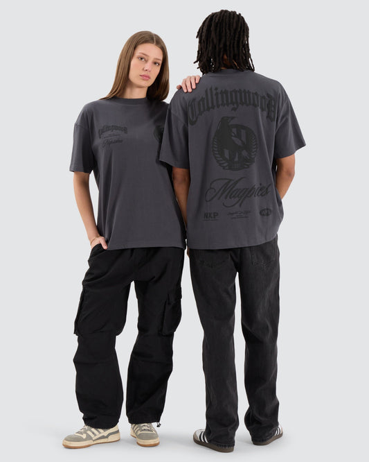Two models wearing the NXP Collingwood T18 Raptor Tee in charcoal, showcasing both the front and back of the oversized AFL Collingwood-themed design.