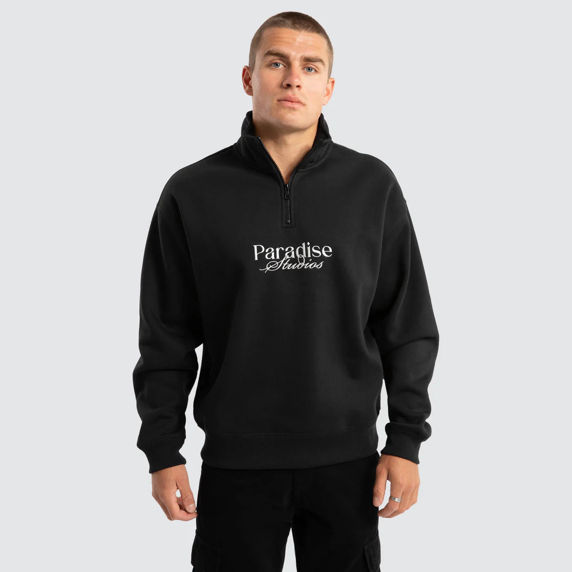Model wearing black Nomadic Merch 1/4 Zip Sweater with white Paradise Studios embroidery