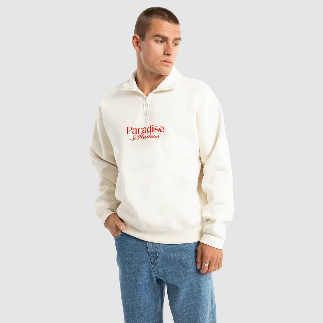 Model wearing off-white Nomadic Merch 1/4 Zip Sweater with red Paradise Studios embroidery